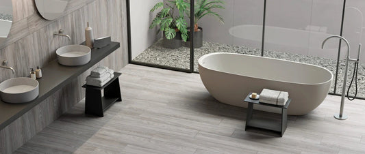 Modern bathroom with grey wood-effect porcelain tile flooring, freestanding bathtub and large window overlooking a garden.