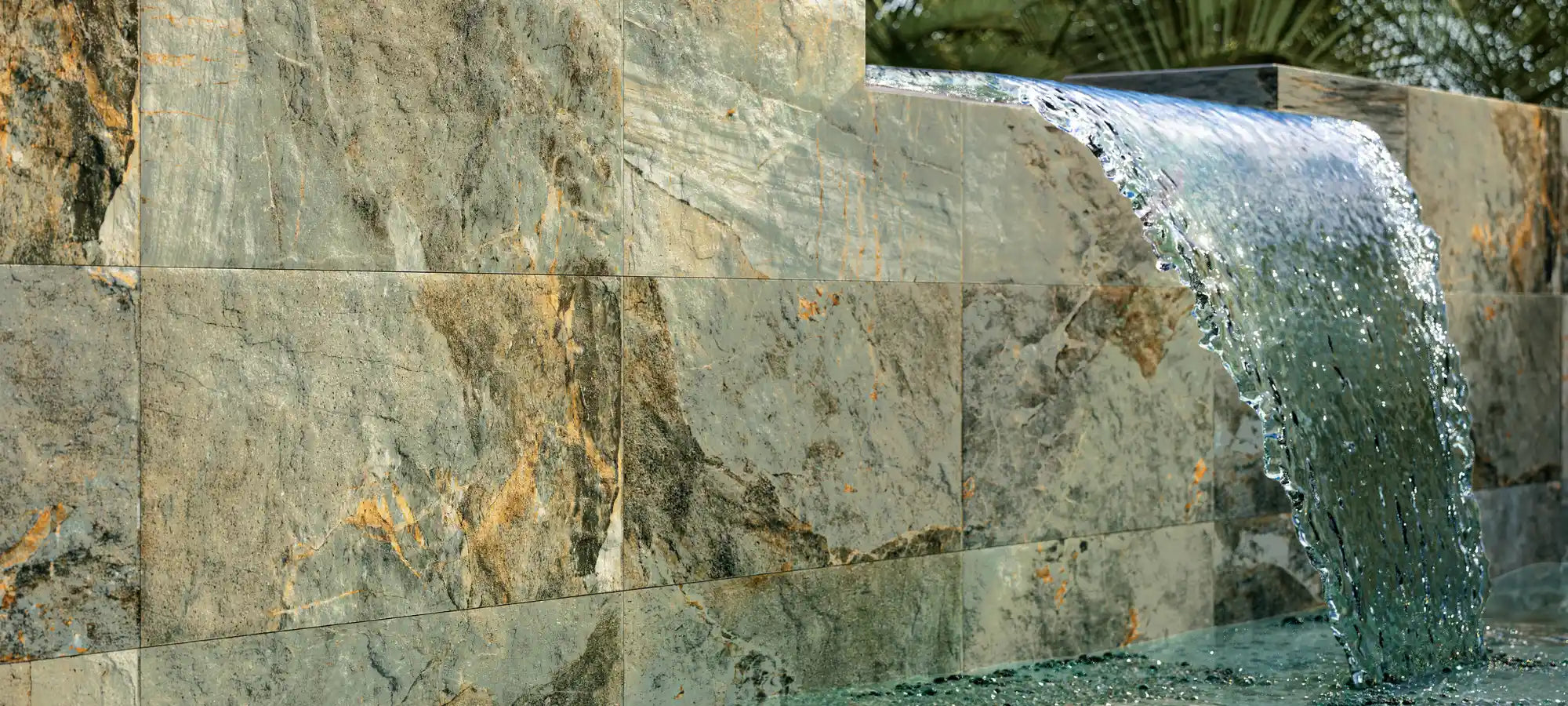 Outdoor wall covered with stone-effect porcelain stoneware tiles featuring a cascading waterfall and natural textures.